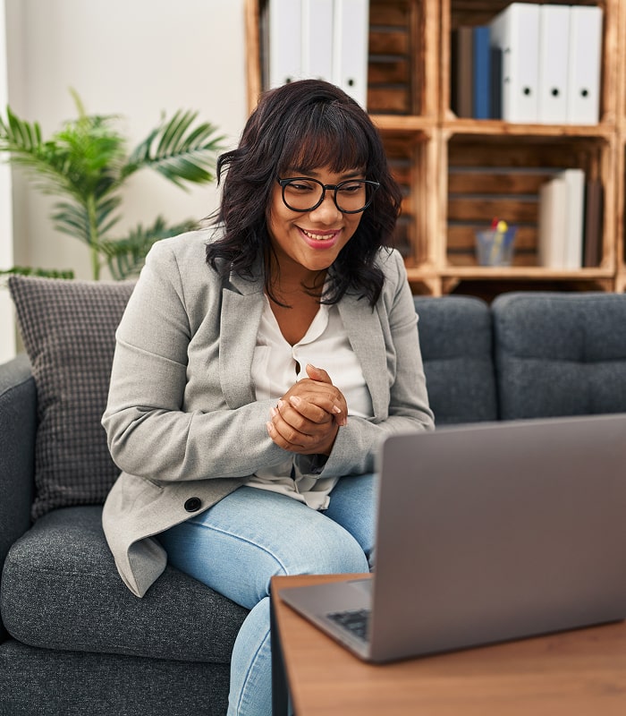 Woman in glasses smiling while participating in an online telehealth session on her laptop.
