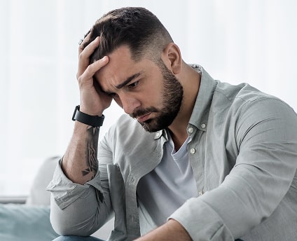 Young man sitting with his hand on his head, looking distressed and overwhelmed, symbolizing anxiety or depression.